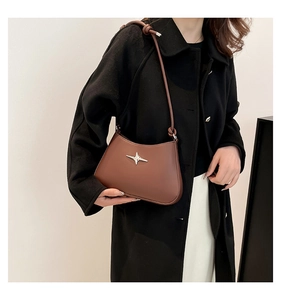 Bolso medialuna de cuero marrón con estrella plateada sobre un abrigo negro de invierno