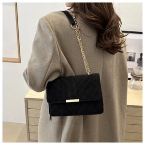 Détail du sac à rabat noir matelassé avec chaîne dorée porté sur un blazer beige chic