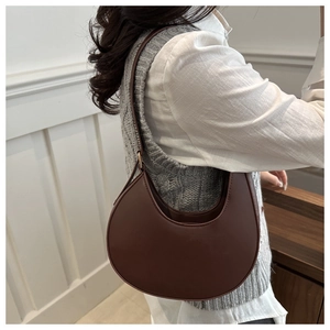 Brown half-moon shoulder bag worn by model against a minimalist interior background