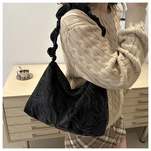 Detail of a black pleated underarm bag featuring a glossy texture and cloud strap