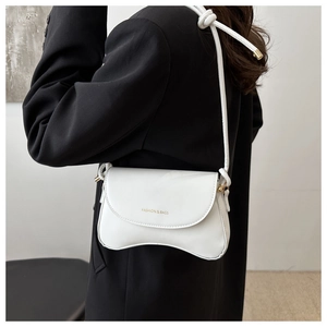Close-up of a white fashion shoulder bag with gold lettering on black clothing background