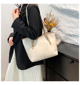 Close-up of beige leather tote bag with brown straps and gold lettering on model
