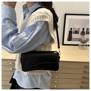 Bolso de hombro minimalista en cuero mate negro con solapa llevado por modelo