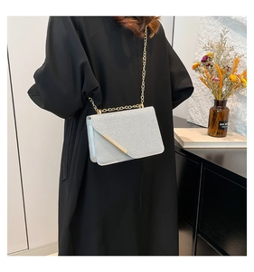 Detail of silver glitter crossbody bag with gold chain strap worn with a black coat