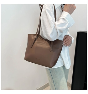 Detail of a dark brown leather tote bag with shoulder strap worn with white shirt