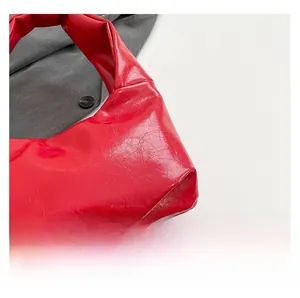 Close-up of vibrant red underarm bag featuring glossy wrinkled leather and rivet details