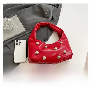Detail of red patent leather underarm bag featuring large silver stud rivets and a sleek finish