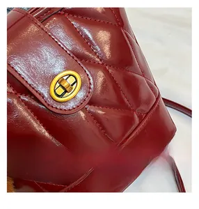 Détail d'un sac seau matelassé rouge foncé en cuir brillant avec fermoir doré tournant