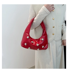 Detail of red patent leather underarm bag with silver rivet studs on a white background