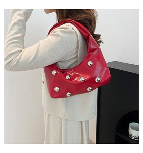 Close-up of a red patent leather hobo bag with silver studs on a white blazer
