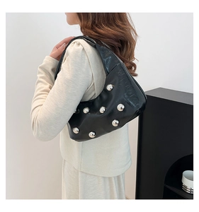 Detail of black patent leather crescent bag featuring bold silver sphere rivets and studs