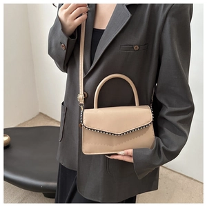 Detail of beige crossbody square bag with silver rivets and sleek top handle strap