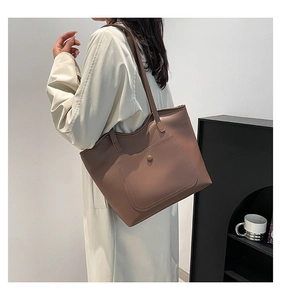 Sac fourre-tout vintage marron porté à l'épaule par un modèle en cuir mat avec poche
