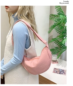 Close-up of pink crescent crossbody bag with pleated texture and adjustable strap