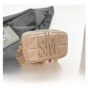 Detail van beige gewatteerde crossbodytas met SM-logo en gouden dubbele ritsen