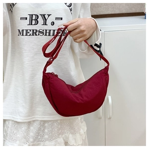 Detail of a dark red crescent crossbody bag with adjustable strap and zipper closure