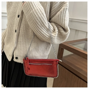 Glossy red shoulder bag with silver studs and chain strap on a knit sweater outfit
