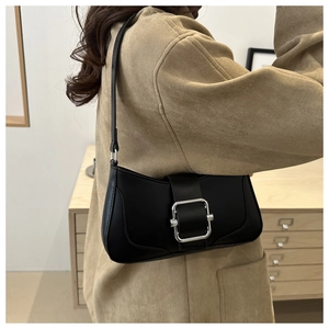 Close-up of minimalist black leather baguette bag with silver buckle on a shoulder