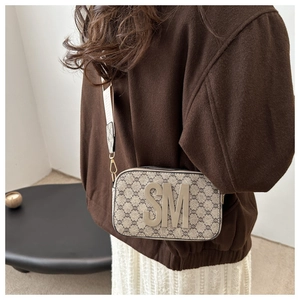 Detail shot of wide logo strap and retro pattern on a canvas crossbody camera bag