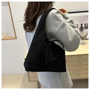 Detail of black suede hobo bag with side bow tie design on shoulder of model