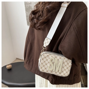 Detail of minimalist crossbody camera bag with beige logo pattern and wide shoulder strap