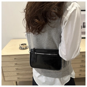 Detail shot of black glossy crossbody bag with silver rivet studs and chain strap