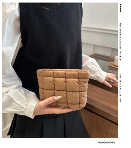 Chic brown quilted puffer pouch with golden zipper shown in a cozy indoor setting