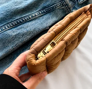 Detail view of the smooth golden metal zipper on the brown quilted nylon makeup bag