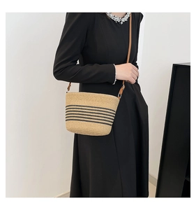 Détail du sac seau en paille beige tissée à la main avec rayures noires et bandoulière