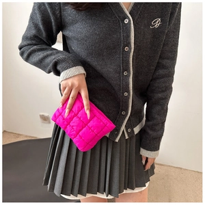 Detailed view of a bright pink quilted puffy clutch bag held by a model for a casual look