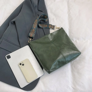 Dark green leather tote bag with a vintage patterned wide shoulder strap on a bed