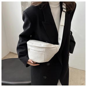 Detail of a beige woven texture crossbody chest bag worn over a black blazer