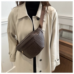 Detail of dark brown woven leather crossbody bag with adjustable strap on beige coat