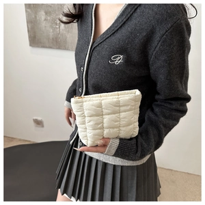 Detail of white quilted clutch bag featuring square padding and a gold zipper closure