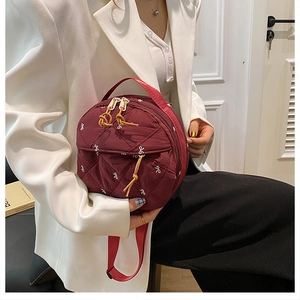 Detail of burgundy quilted round bag with white bow embroidery and double zippers