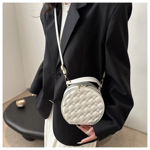 Detail of white round crossbody bag featuring woven texture and gold metal zipper hardware