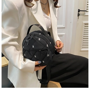 Detail of black quilted mini bag with white bow embroidery and top handle on a white blazer