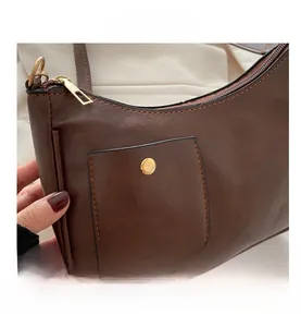 Detail of dark brown leather crescent bag showing gold metal zipper and front pocket