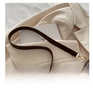 Detail of dark brown leather shoulder strap with gold metal swivel hook on cream blazer
