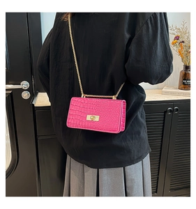 Detail of fuchsia crocodile pattern box bag with gold chain strap on a female model