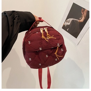 Detail of burgundy quilted mini backpack with white bow embroidery and double zippers