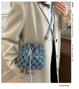 Détail du sac seau en denim damier bleu avec fermeture à cordon et boucles dorées