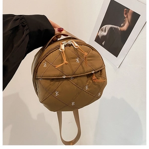 Detailed view of brown quilted round bag featuring white bow embroidery and orange pullers