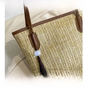 Detail of woven straw tote bag with brown leather trim and decorative tassel pendant