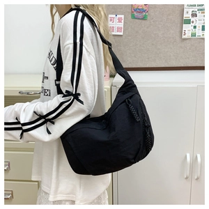 Detail of black crossbody dumpling bag featuring wide strap and woven zipper pull cord