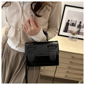 Vue détaillée d'un sac à main carré en cuir noir avec tenue minimaliste et décor en bois clair