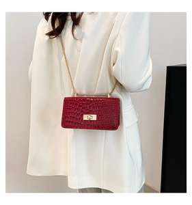 Detail of red crocodile pattern patent leather box bag with gold chain on white suit