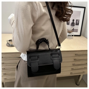 Détail du sac bandoulière noir avec poignée plissée et boucles carrées porté par un mannequin