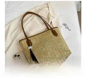Detail of straw tote with leather trim and fringe tassel shown next to a smartphone