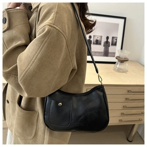 Detail shot of a black crescent shoulder bag with golden buckle on a textured leather pocket
